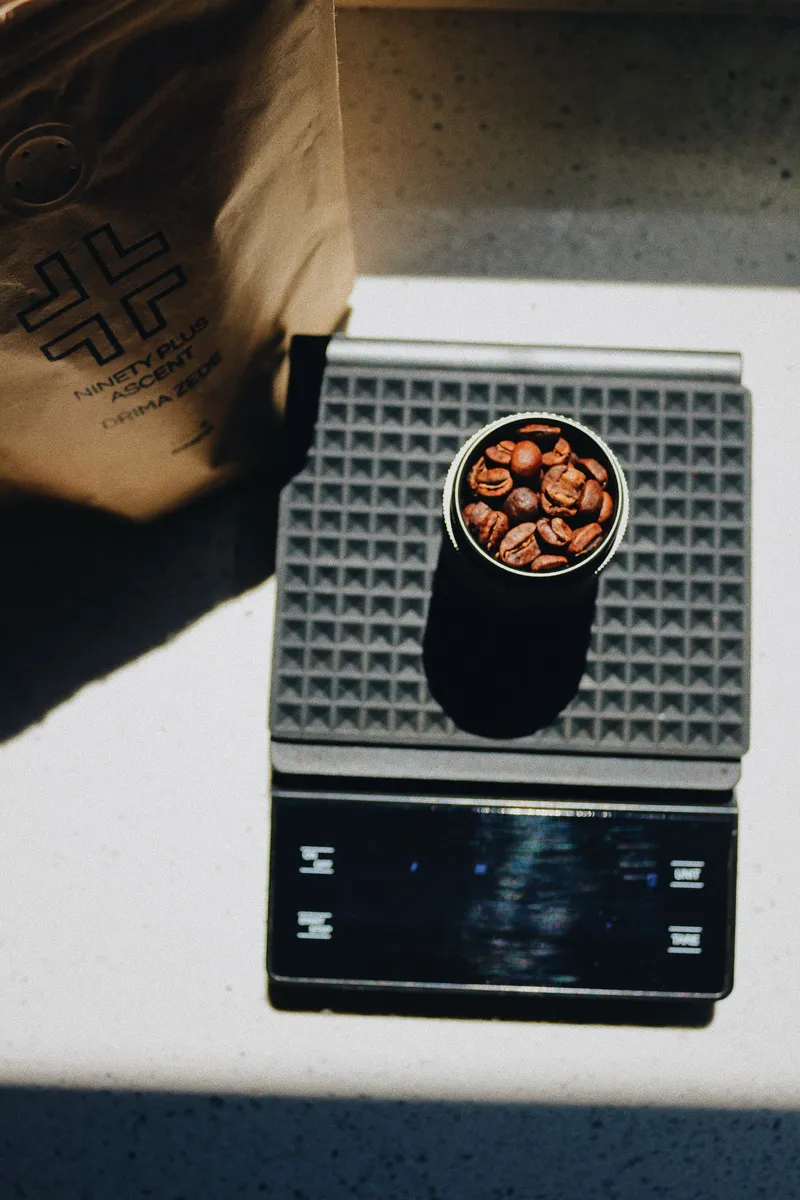 Granos de café pesándose en una báscula digital de precisión junto a una jarra