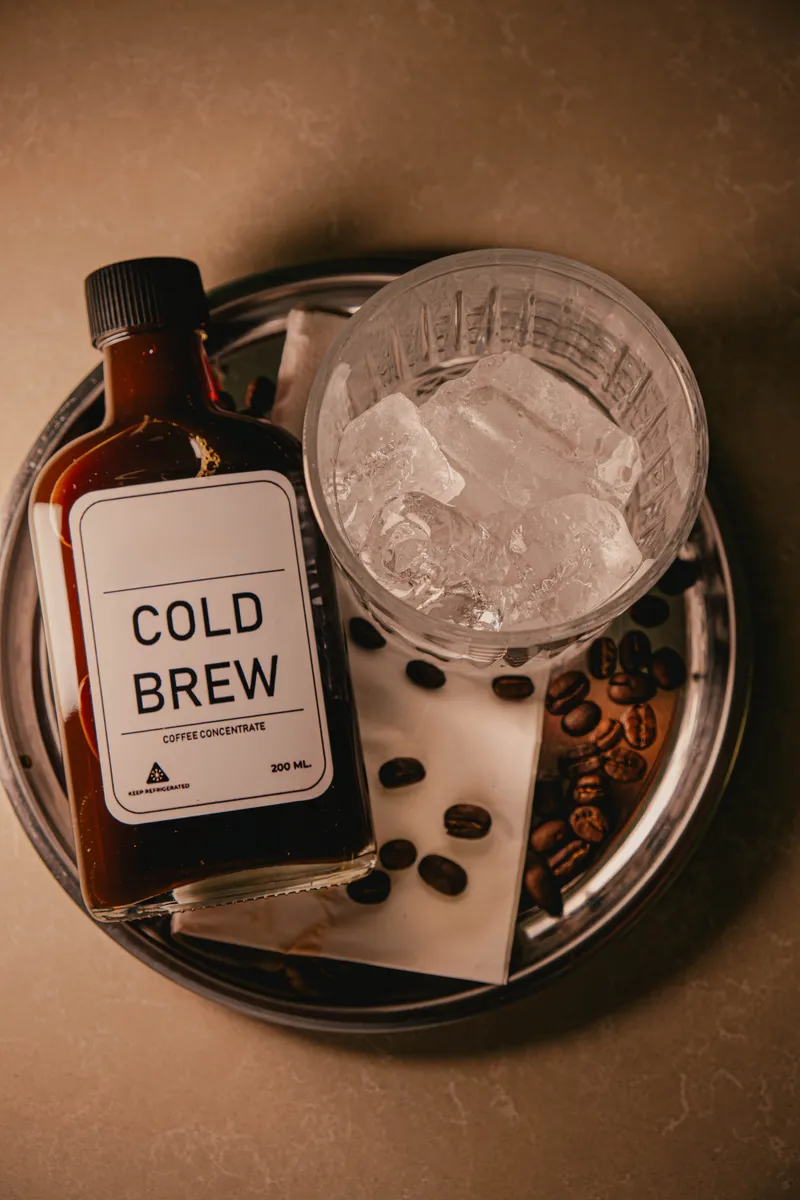 Botella de concentrado de cold brew junto a un vaso con hielo sobre una bandeja