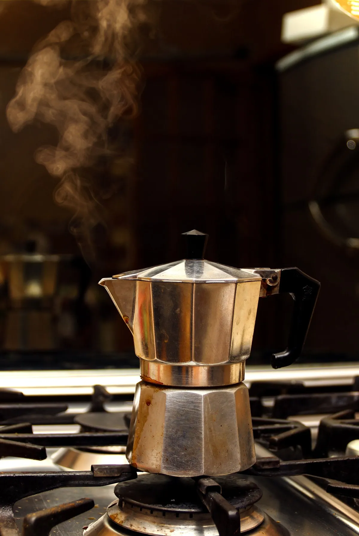 Cafetera italiana moka humeante sobre el fuego de la cocina